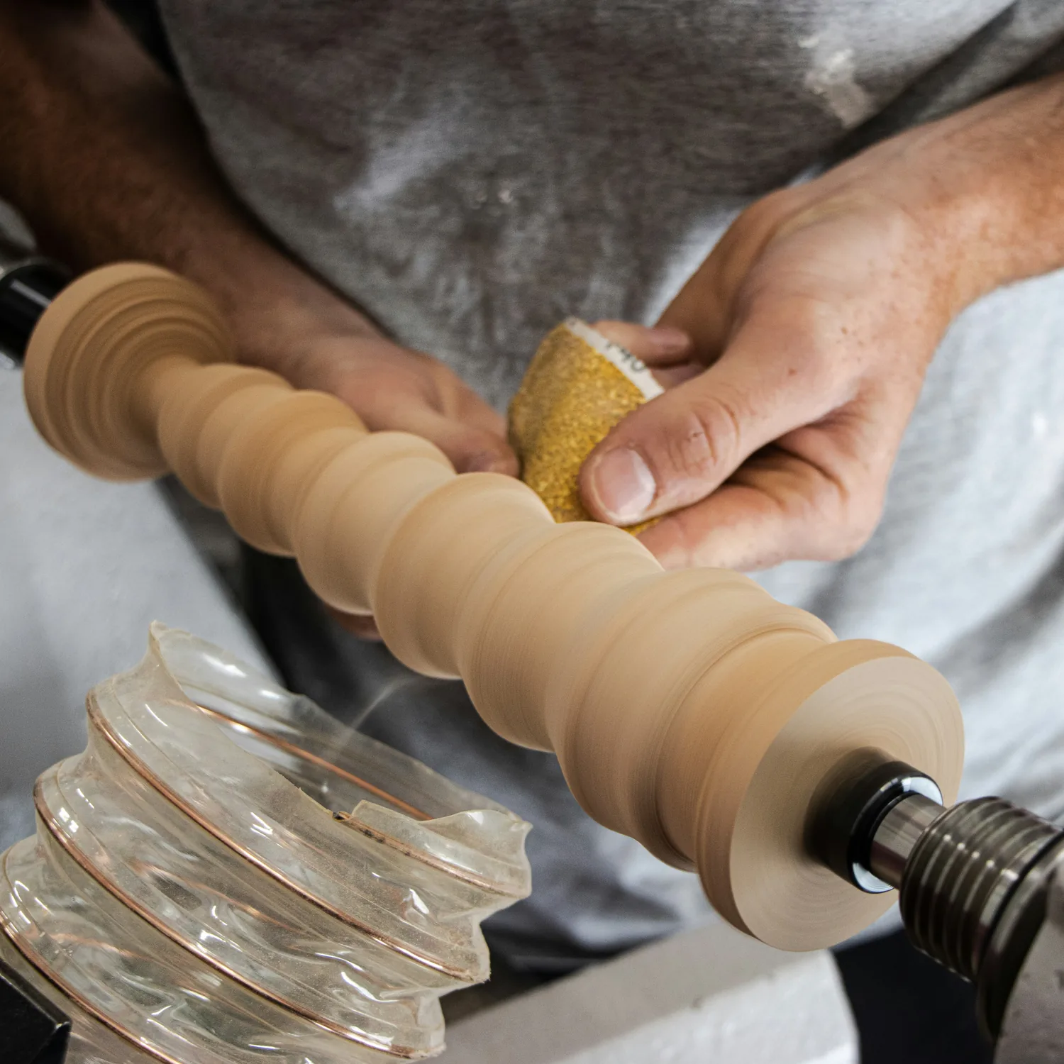 Hands sanding a turned wooden piece on a lathe